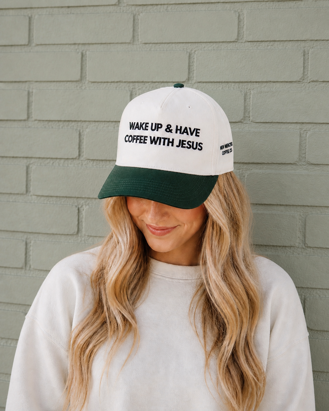 Person wearing a cap with 'Wake Up & Have Coffee With Jesus' text against a brick wall.