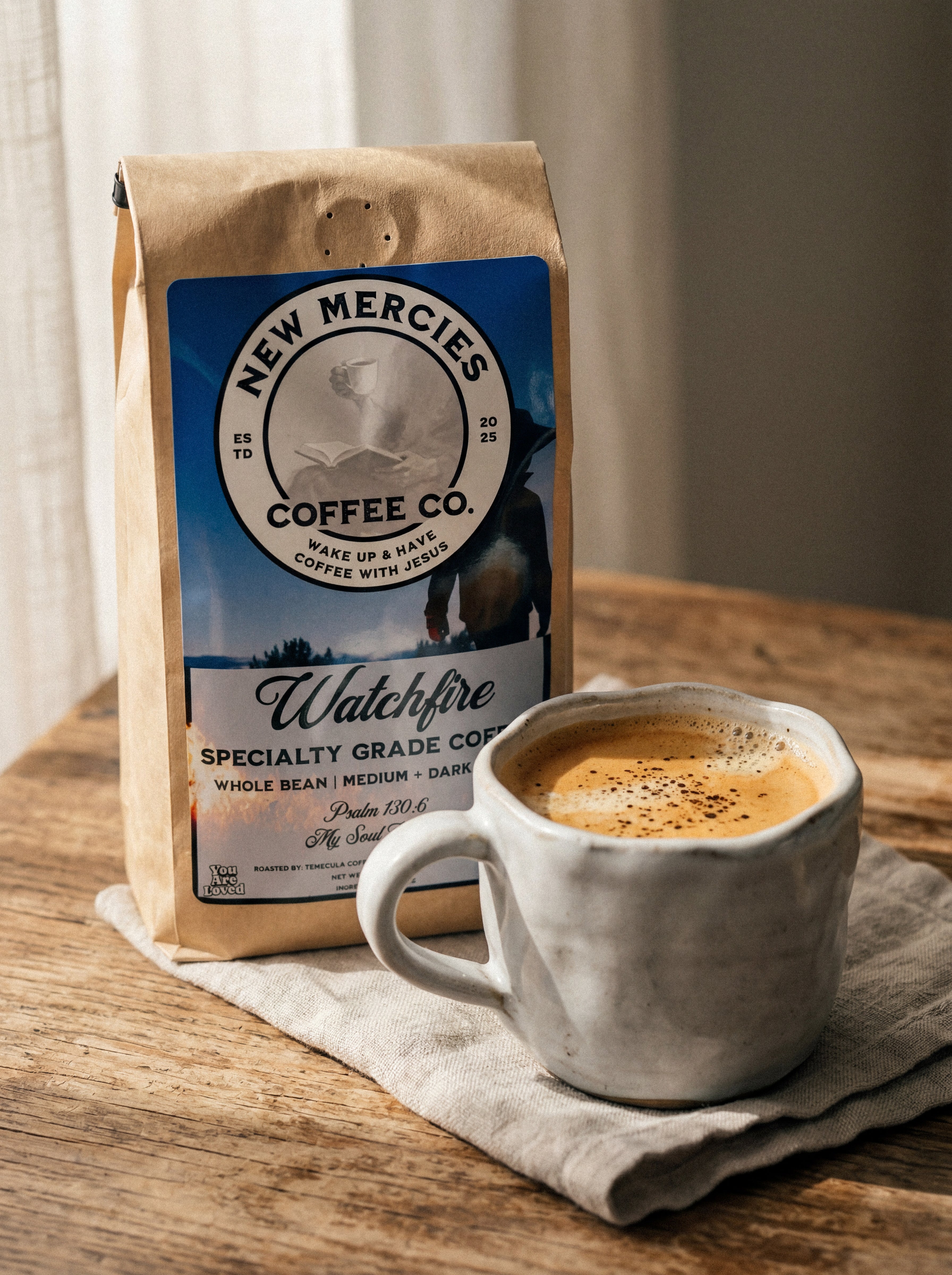 New Mercies Coffee Co. bag with a cup of coffee on a wooden table