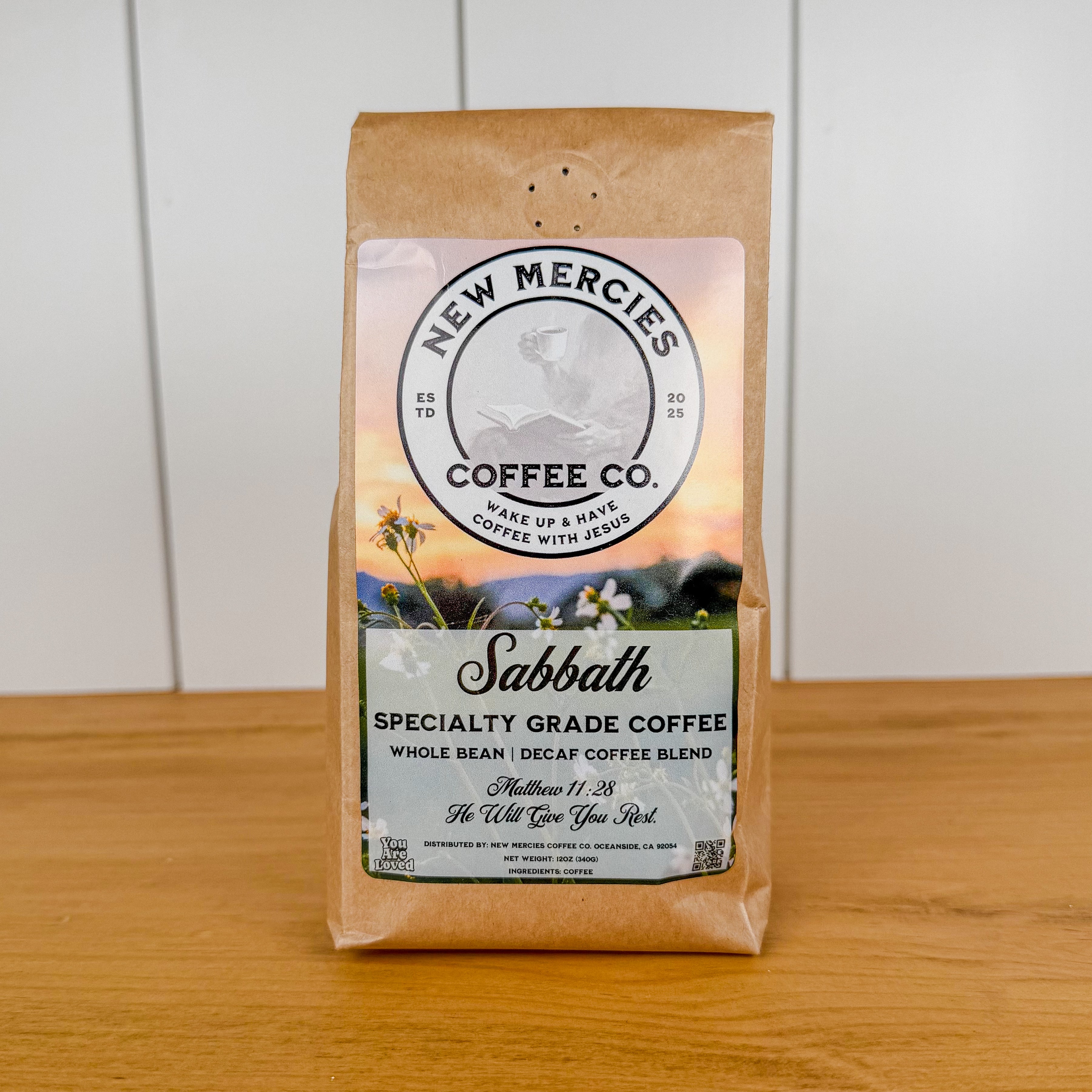 Coffee bag from New Mercies Coffee Co. on a wooden surface with a white background